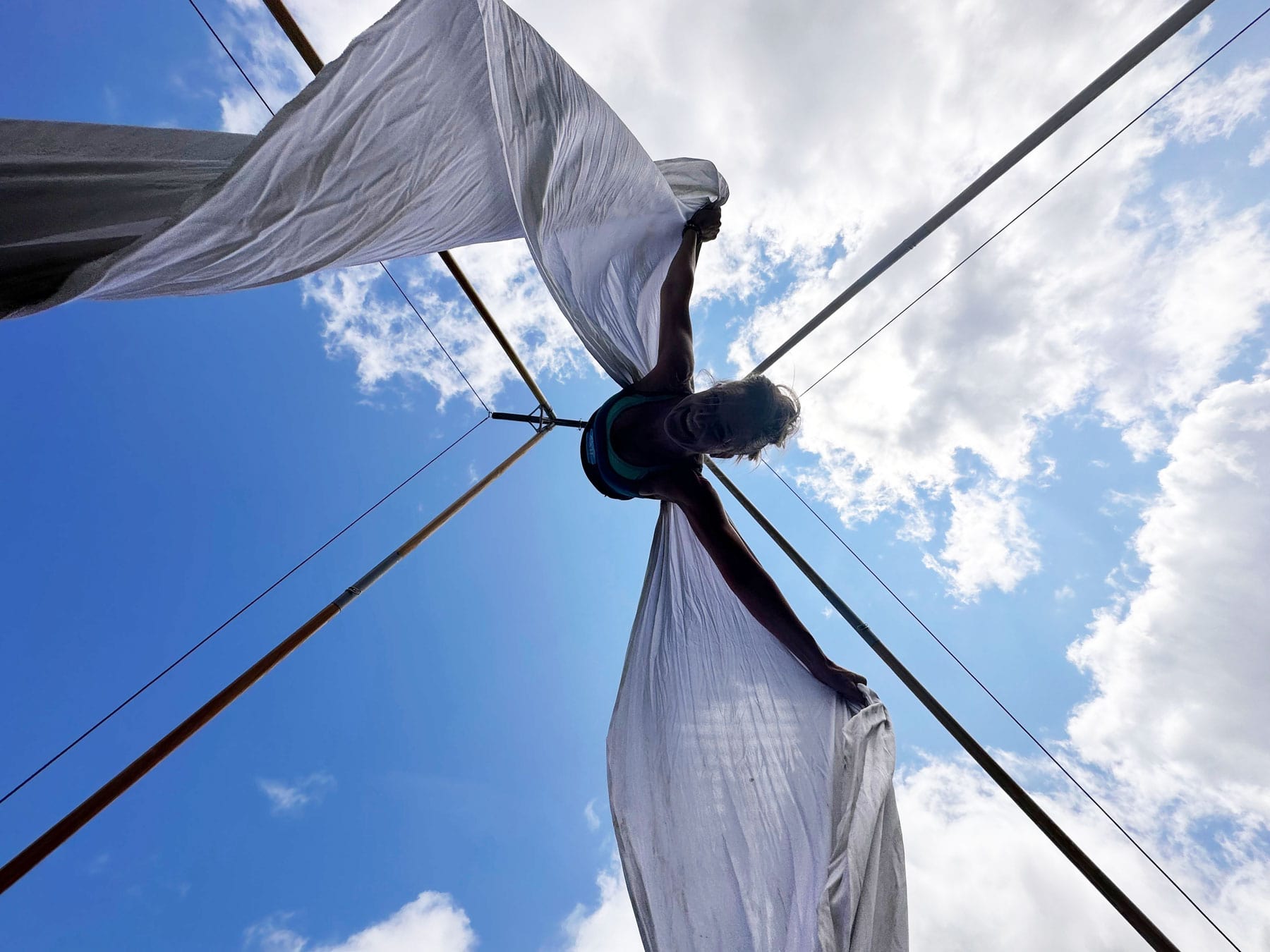 Debbie is hanging upside down smiling from the Air Frame using silks